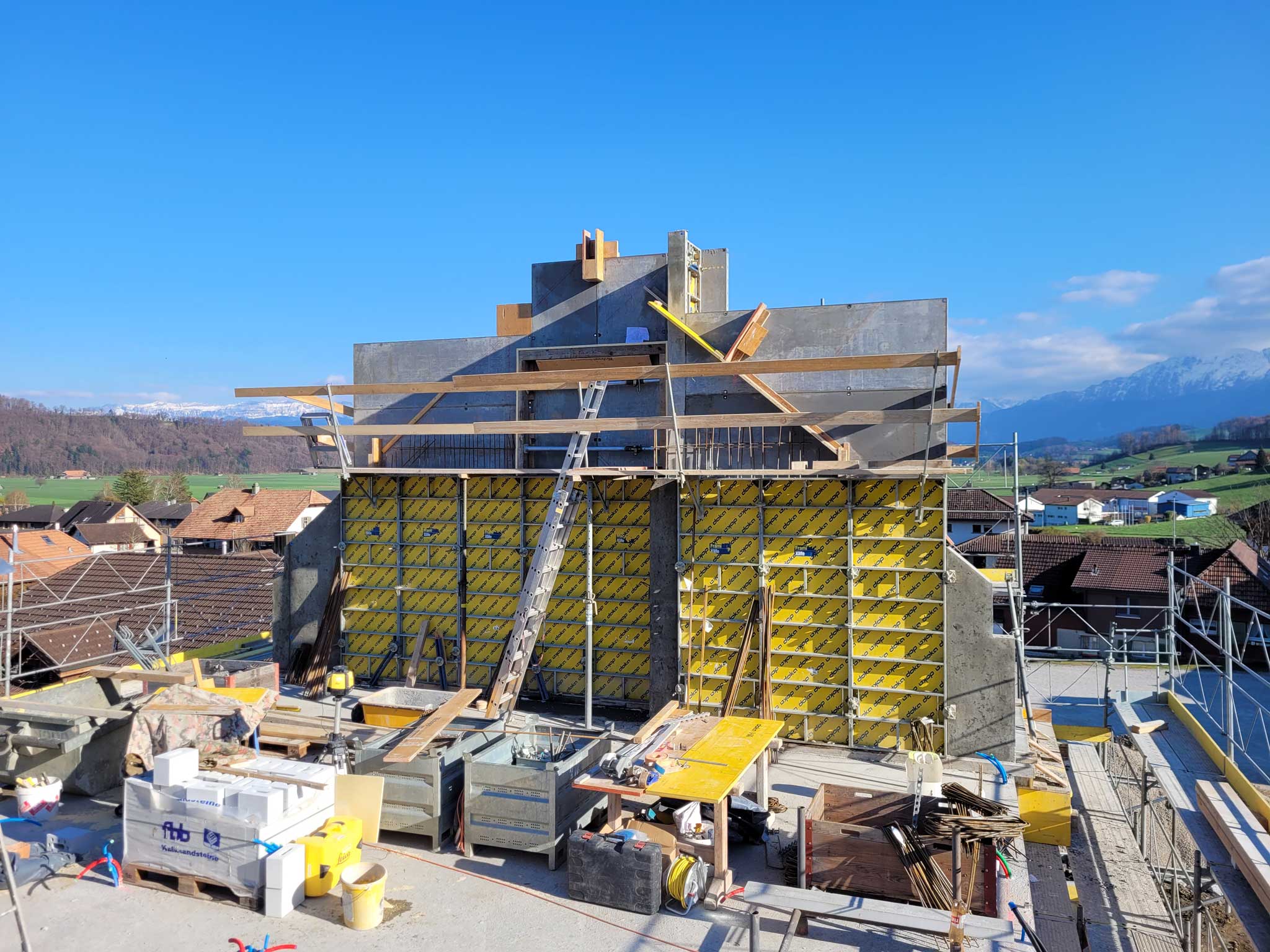 Neubau mit gelber Schalung vor den Berner Alpen.
