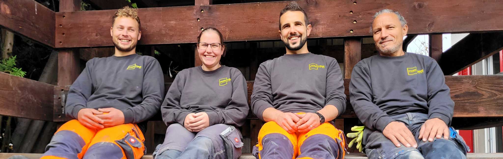 Das Team der Portner Bau AG sitzt in Arbeitskleidung auf einer Holzbank.